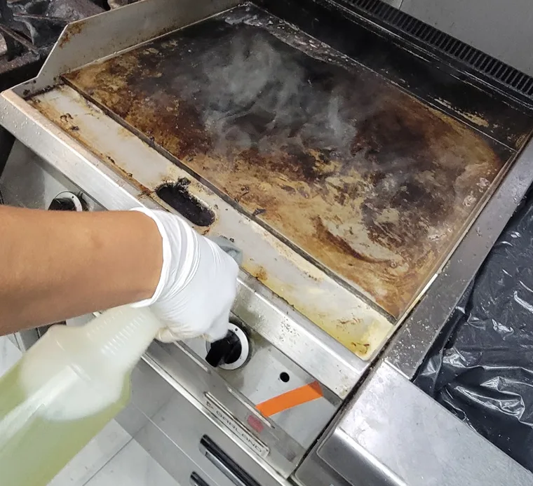 Commercial Restaurant Cleaning services staff degreasing a stainless steel restaurant flat-top grill.
