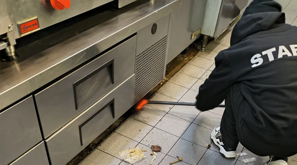 CSIK staff member deep cleaning under commercial kitchen equipment in a restaurant