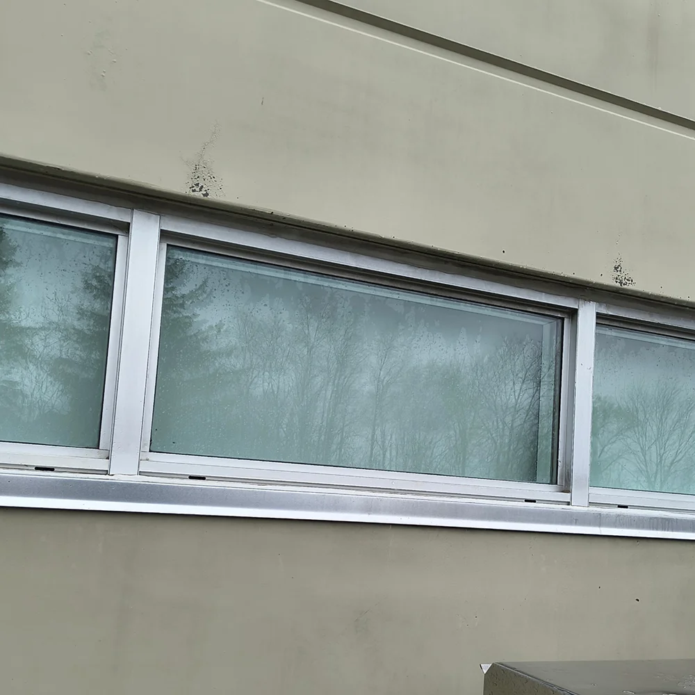 A close-up shot of the same commercial building exterior wall after pressure washing, demonstrating a clean, stain-free facade above aluminum-framed windows following exterior restoration services by CSIK.
