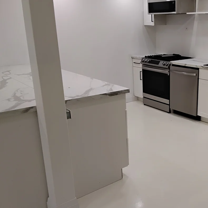 A wide interior shot of the same modern kitchen fully cleaned, organized, and sanitized, showing spotless white marble-patterned countertops, gleaming stainless steel appliances, and polished white flooring following residential deep cleaning services by CSIK.